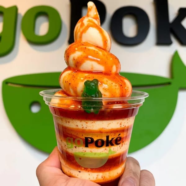A GoPoke soft serve dessert with chili sauce and a green gummy bear, held in front of a green logo.