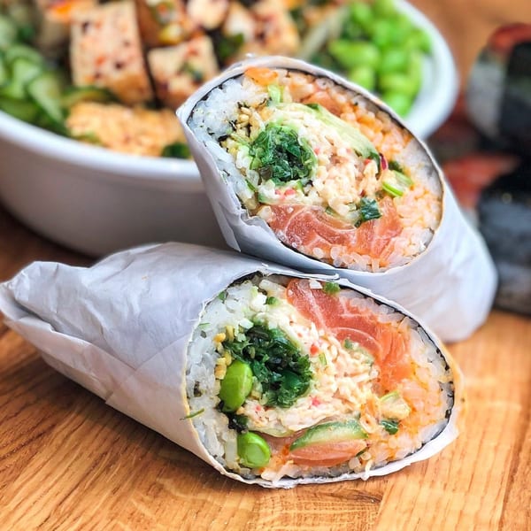 Two GoPoke sushi burritos, cut in half, revealing salmon, rice, avocado, and seaweed on a wooden table.