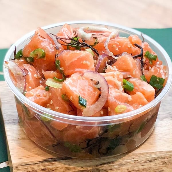 GoPoke salmon poke bowl with red onions, green onions, and seaweed on a wooden surface.