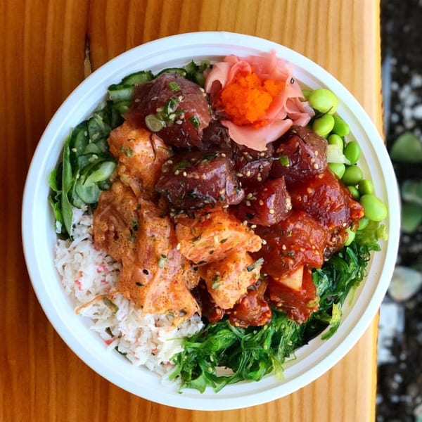 A vibrant GoPoke bowl with various poke, rice, crab salad, seaweed, edamame, and pickled ginger.
